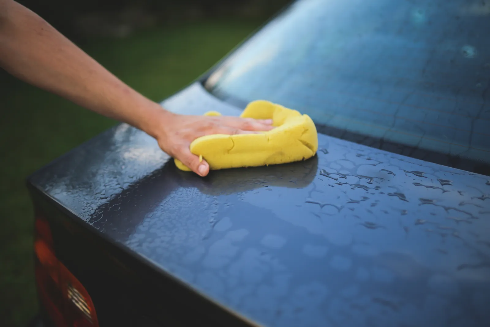 Hand wiping a wet black car with a yellow sponge during an exterior detail